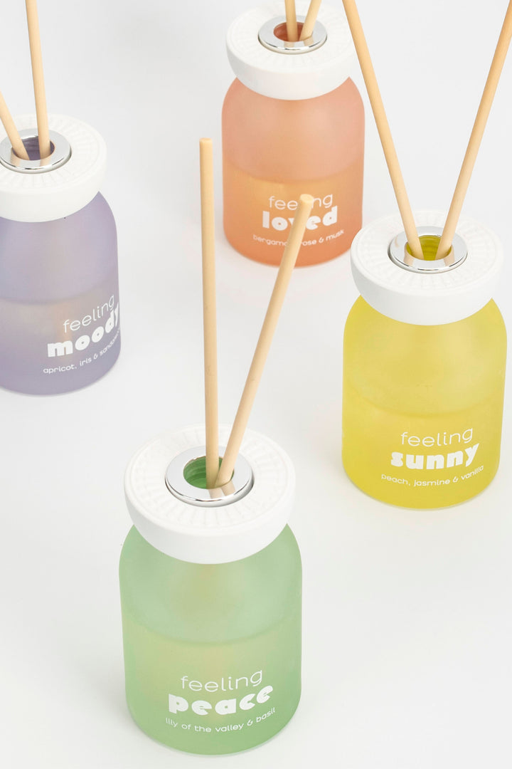 Four diffuser bottles with sticks labeled 'feeling loved', 'feeling peace', 'feeling sunny', and 'feeling good' on a white background.