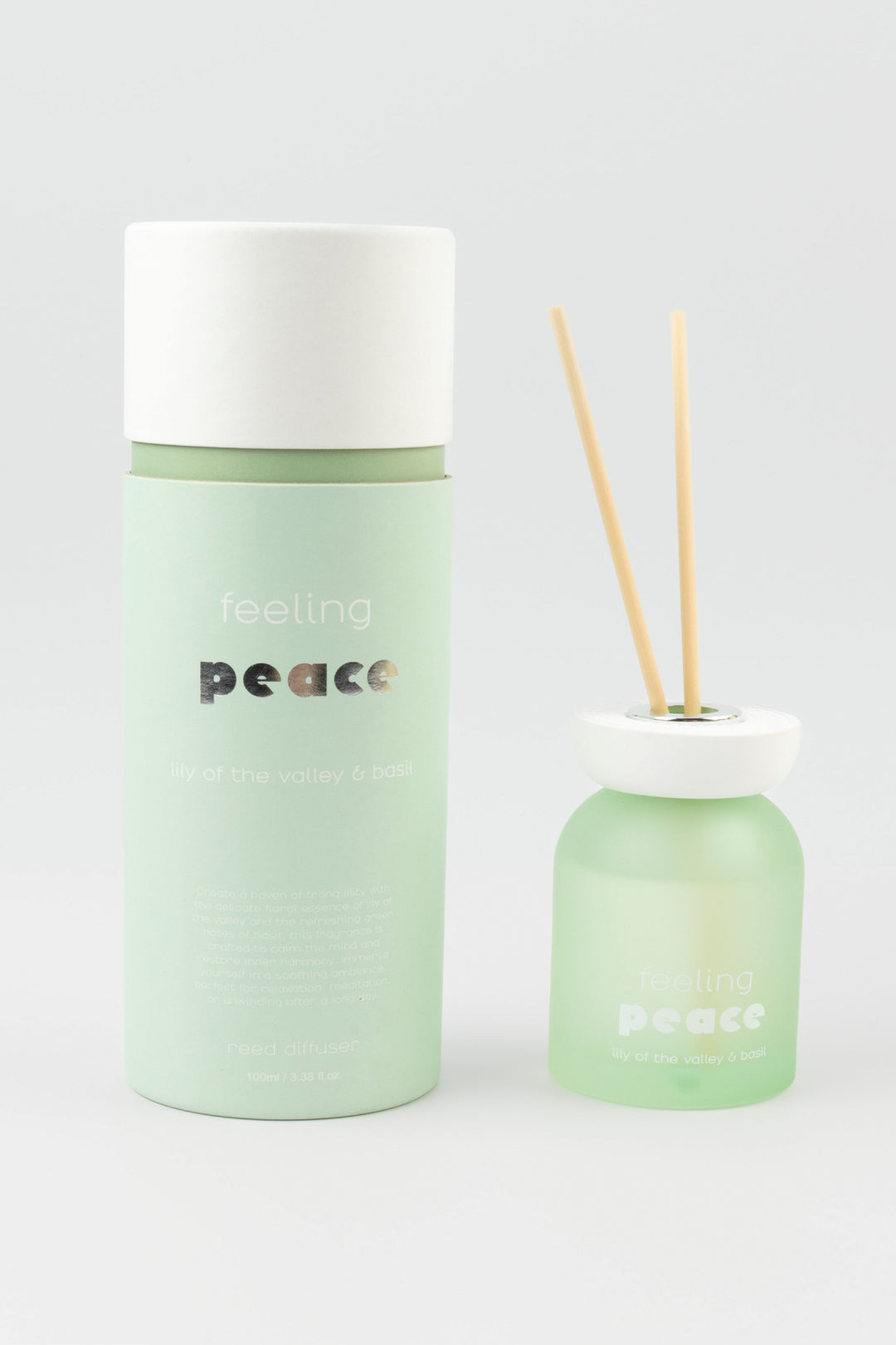 Green diffuser bottle with white cap and wooden sticks on a light gray background