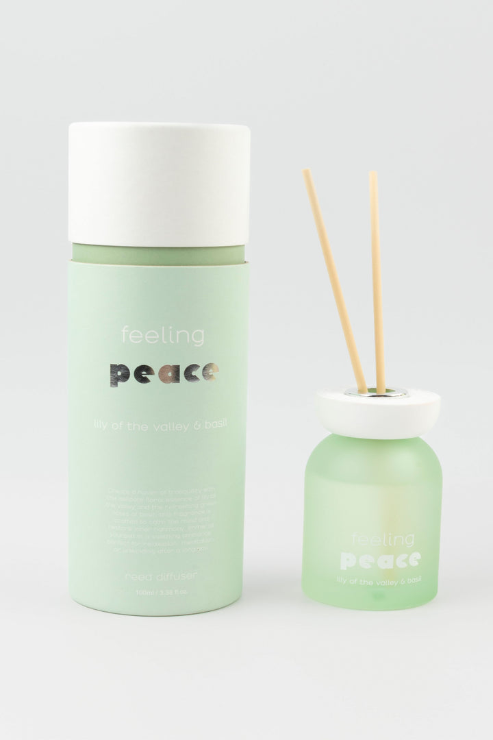 Green diffuser bottle with white cap and wooden sticks on a light gray background