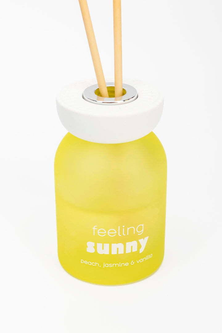 Yellow diffuser bottle labeled 'feeling sunny' with wooden sticks on a white background