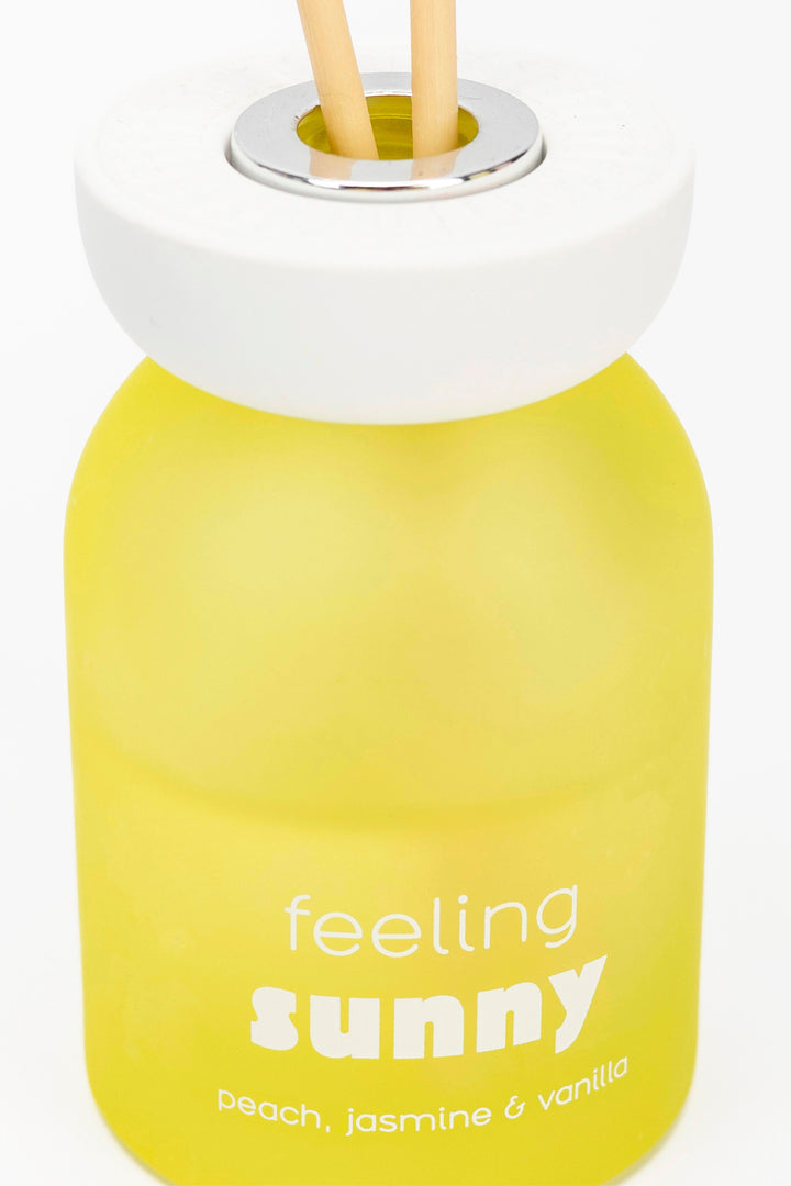 Yellow bottle with 'feeling sunny' text and wooden sticks on a white background