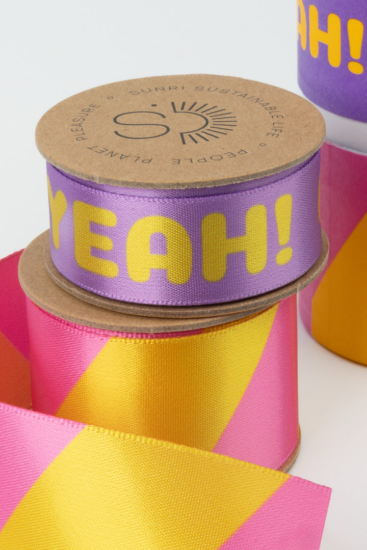 Spool of purple ribbon with yellow text 'YEAH!' on a pink background