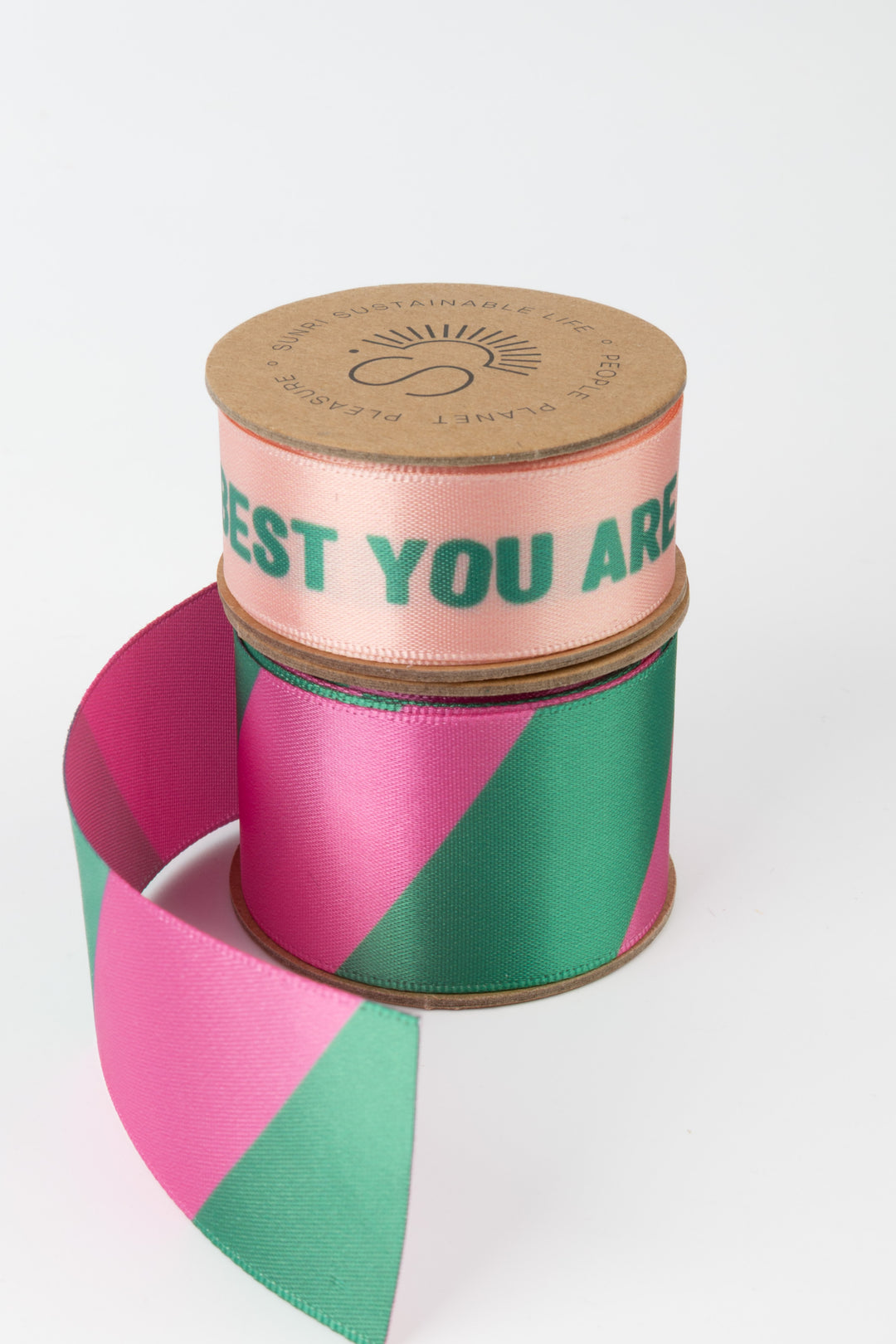 two satin ribbon rolls stacked one yellow printed text and one pastel geometric printed ribbon partially unrolled on white surface
