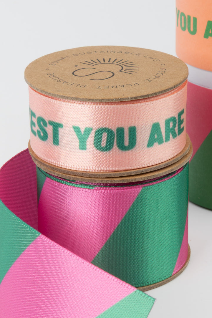 close view of satin ribbon rolls showing green printed messaging and geometric patterned ribbon on cardboard cores
