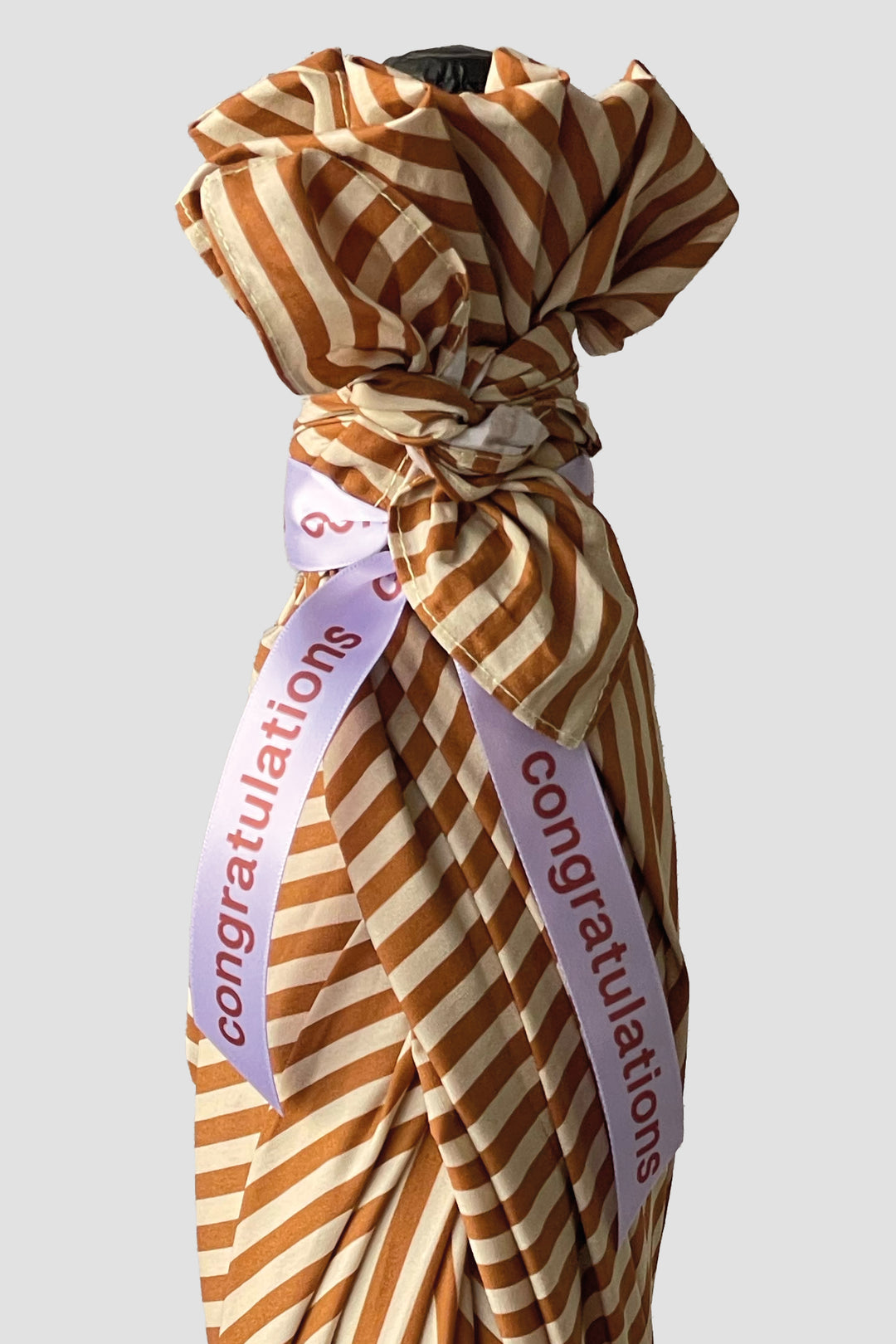 Striped furoshiki wrapping with 'Congratulations' ribbon on a light gray background