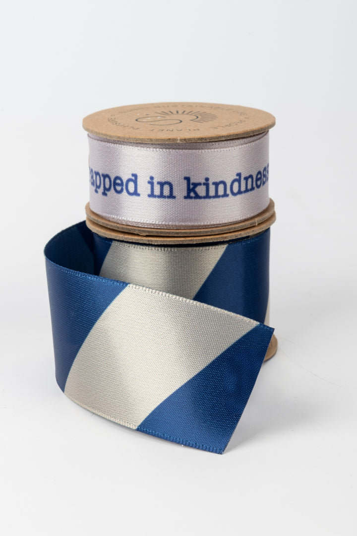 Blue and white ribbon with a cartboard spool labeled 'Wrapped in kindness' on a white background