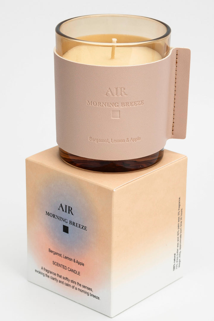 Candle labeled 'AIR Morning Breeze' on a matching box with a beige background