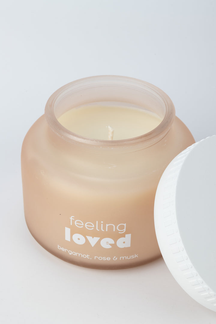 Candle in a jar labeled 'feeling loved' on a white background