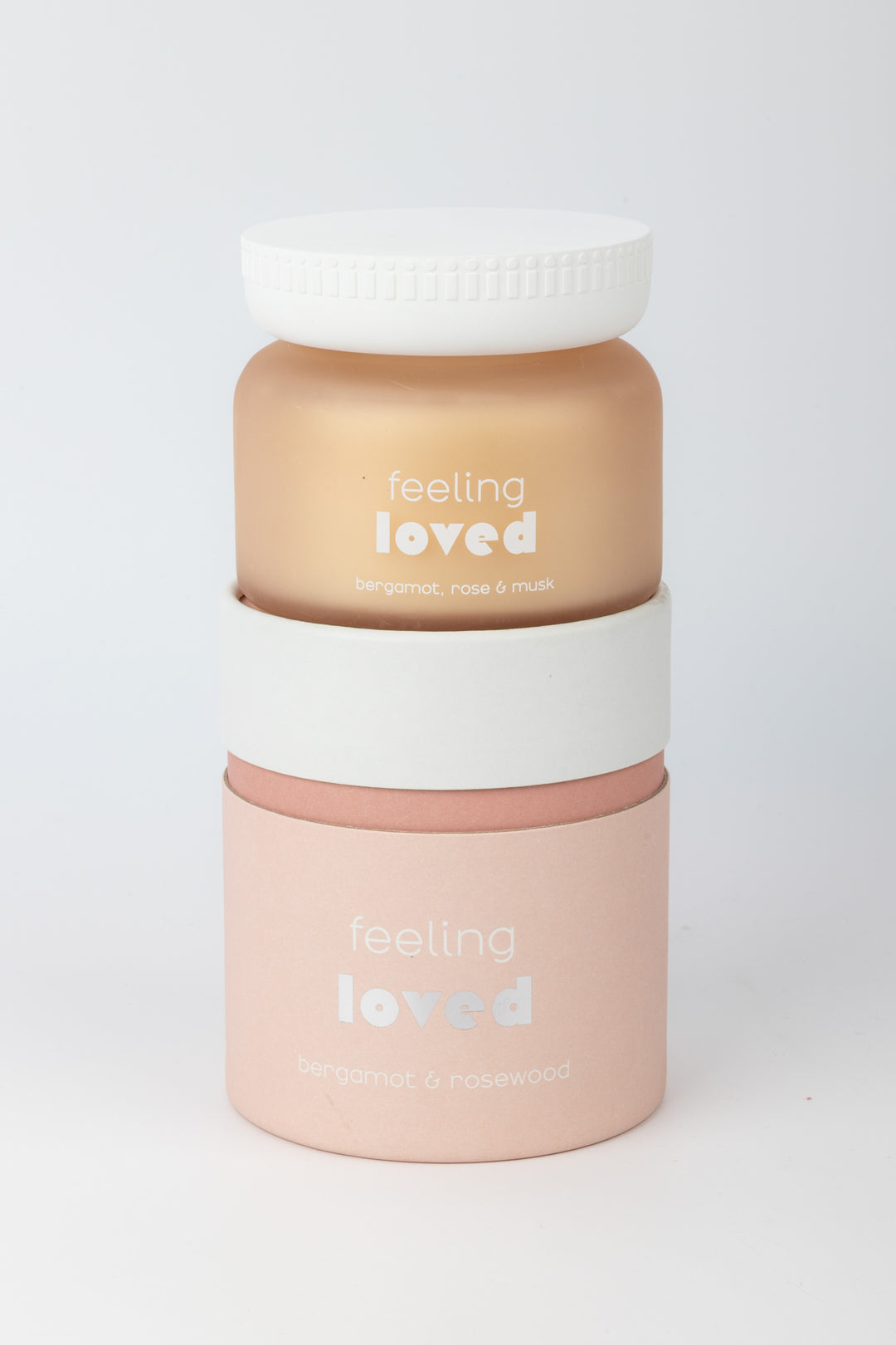 Candle with 'feeling loved' text stacked on cilindric packaging on a white background