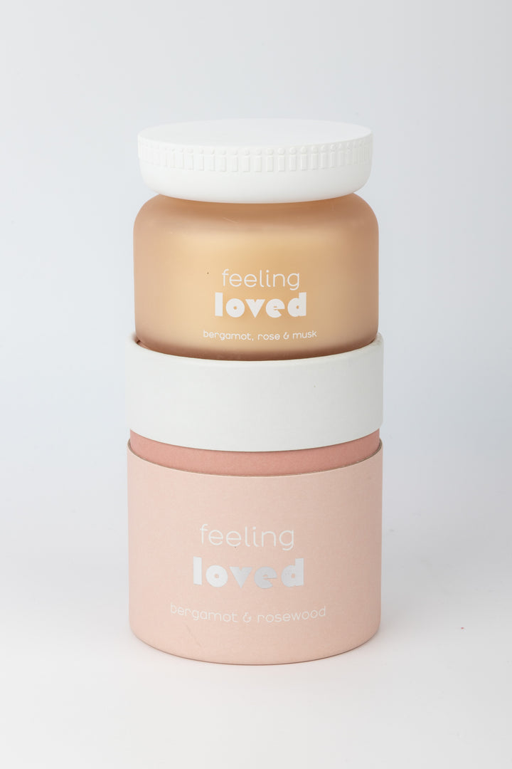Candle with 'feeling loved' text stacked on cilindric packaging on a white background
