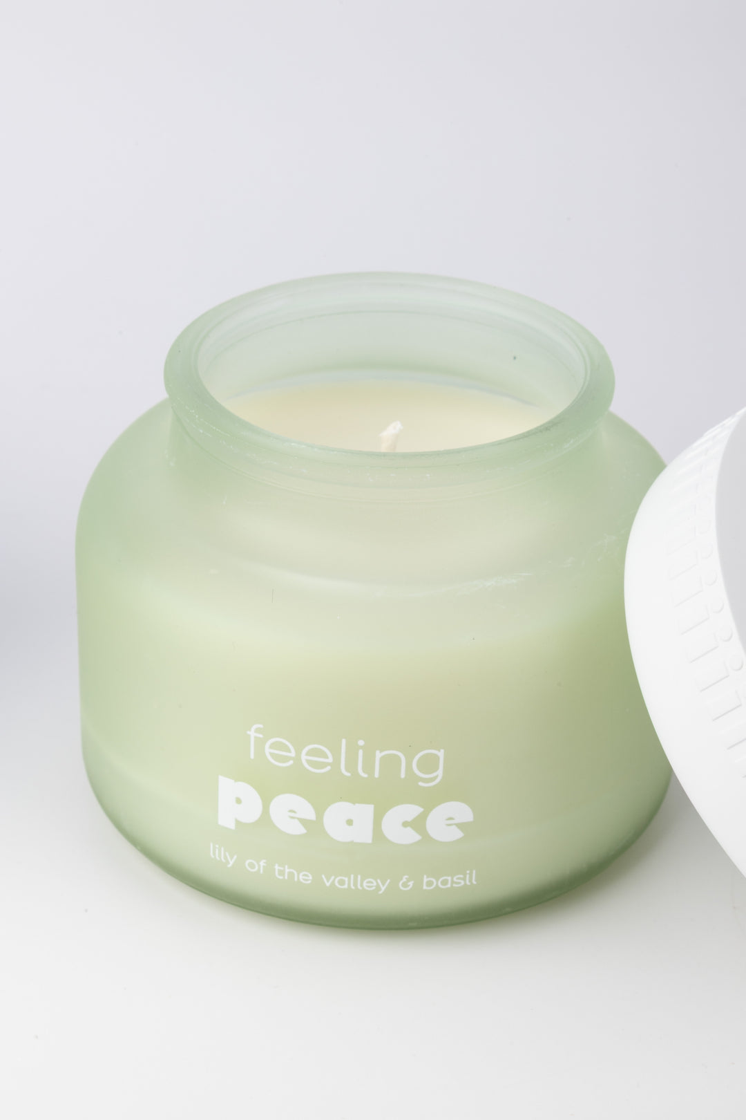 Green candle jar labeled 'feeling peace' on a white background