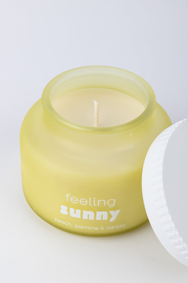 Yellow candle labeled 'feeling sunny' with a white lid on a light background