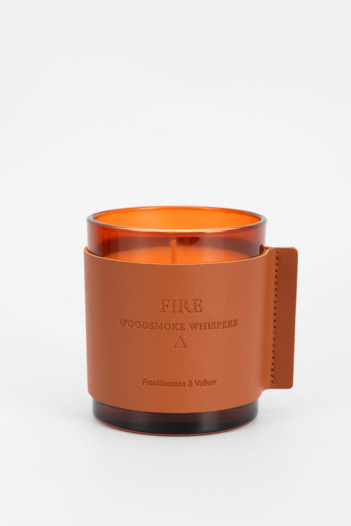 Candle with orange interior and brown leather holder on a white background