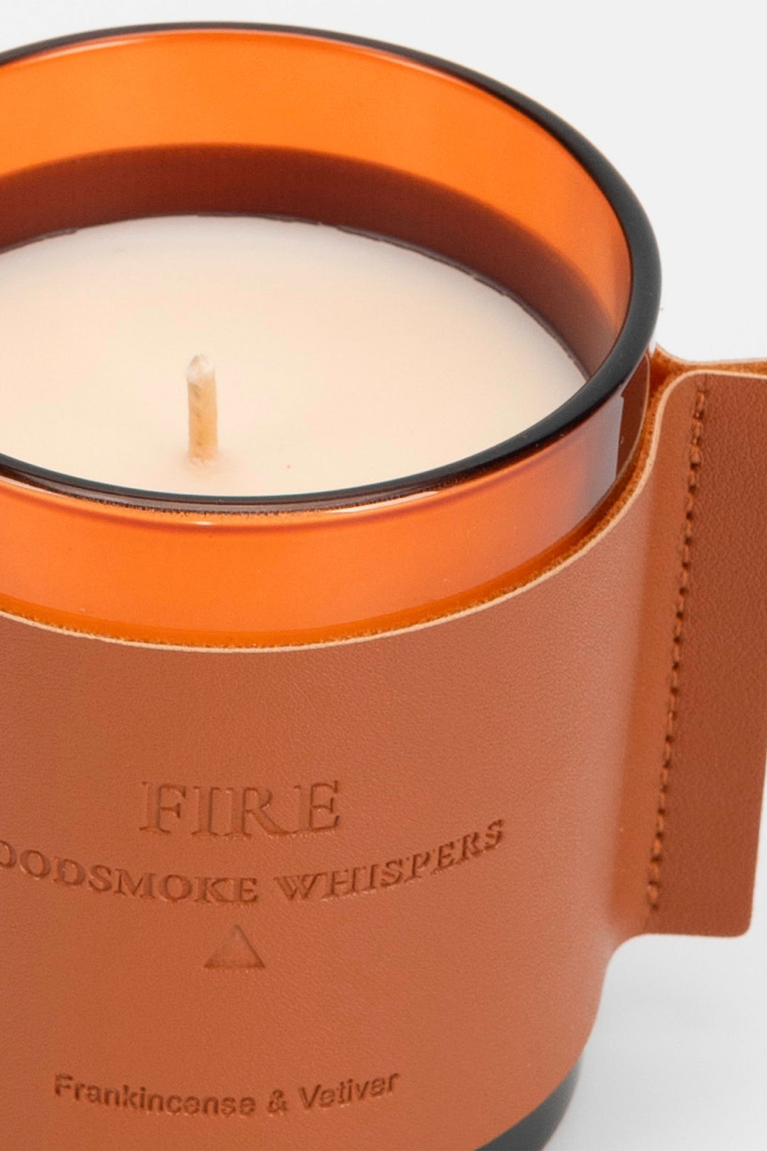 Candle in an orange holder with 'Fire Woodsmoke Whispers' text on a white background