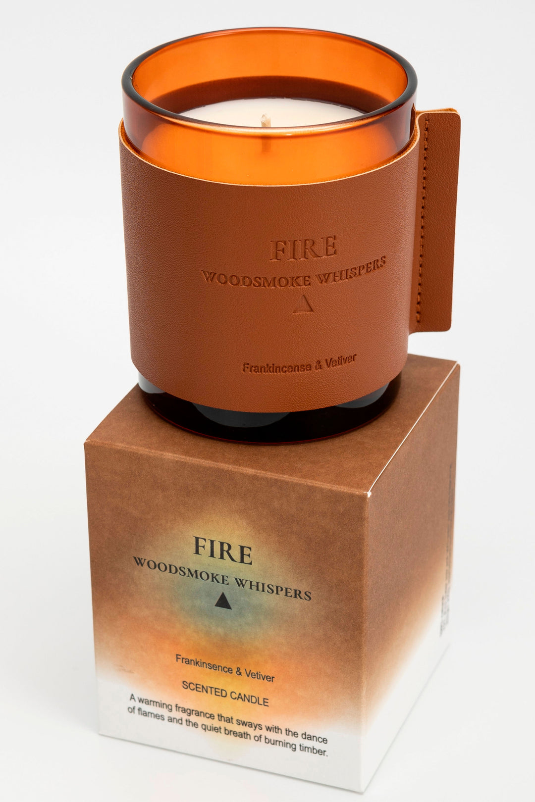 Candle with orange lid and leather-wrapped base on a white background
