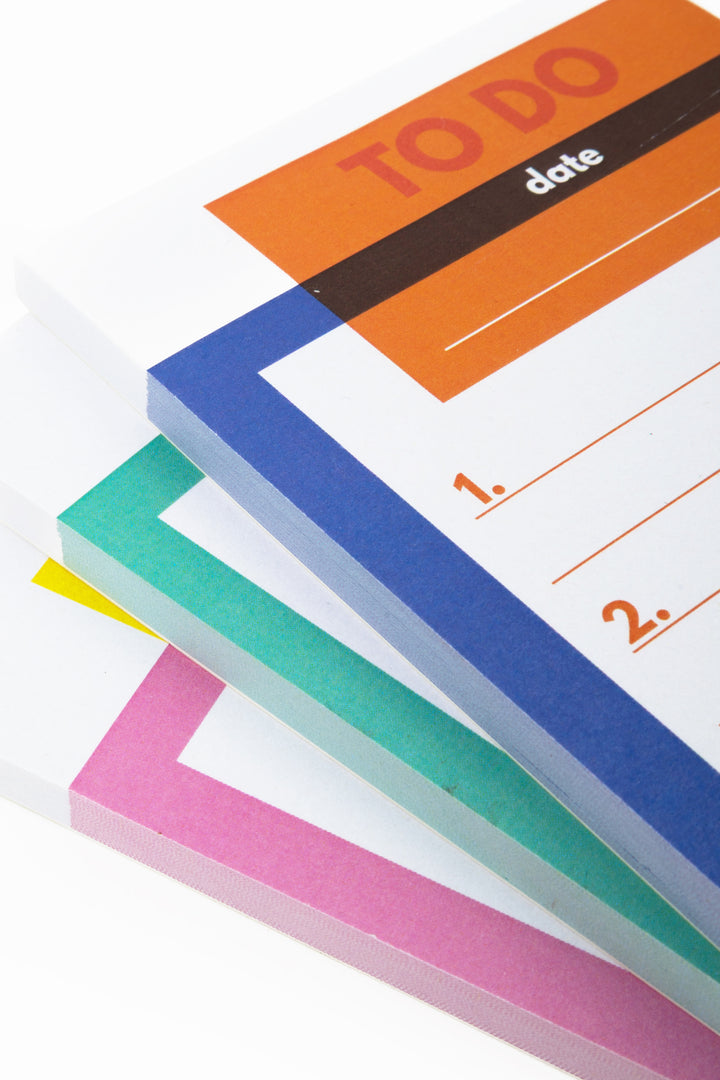 Stacked colour-blocked notepads showing the blue, green, yellow and pink edges
