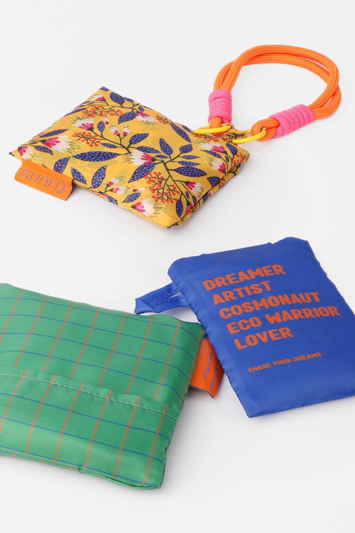 Three colourful folded shopping bags in pouches with different designs and text 