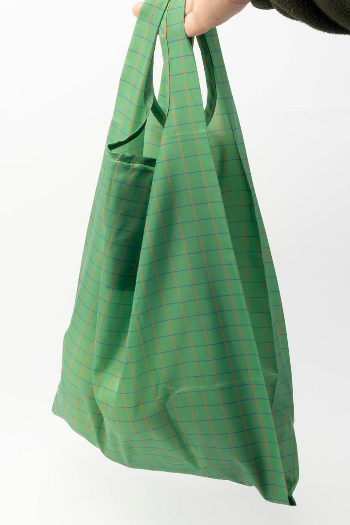 Green plaid large reusable bag held by a hand on a white background