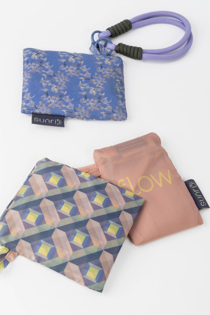 Three colourful folded shopping bags in pouches with different designs and text 