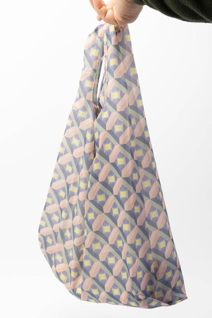 Patterned reusable shopping bag held by a hand on a white background