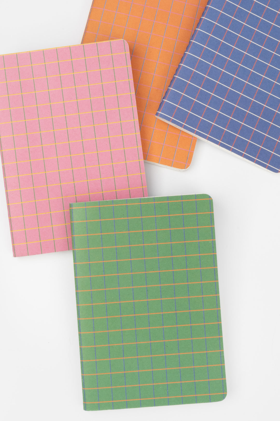 four mini notebooks in pink, blue, orange and green with grid covers arranged in a diagonal overlap
