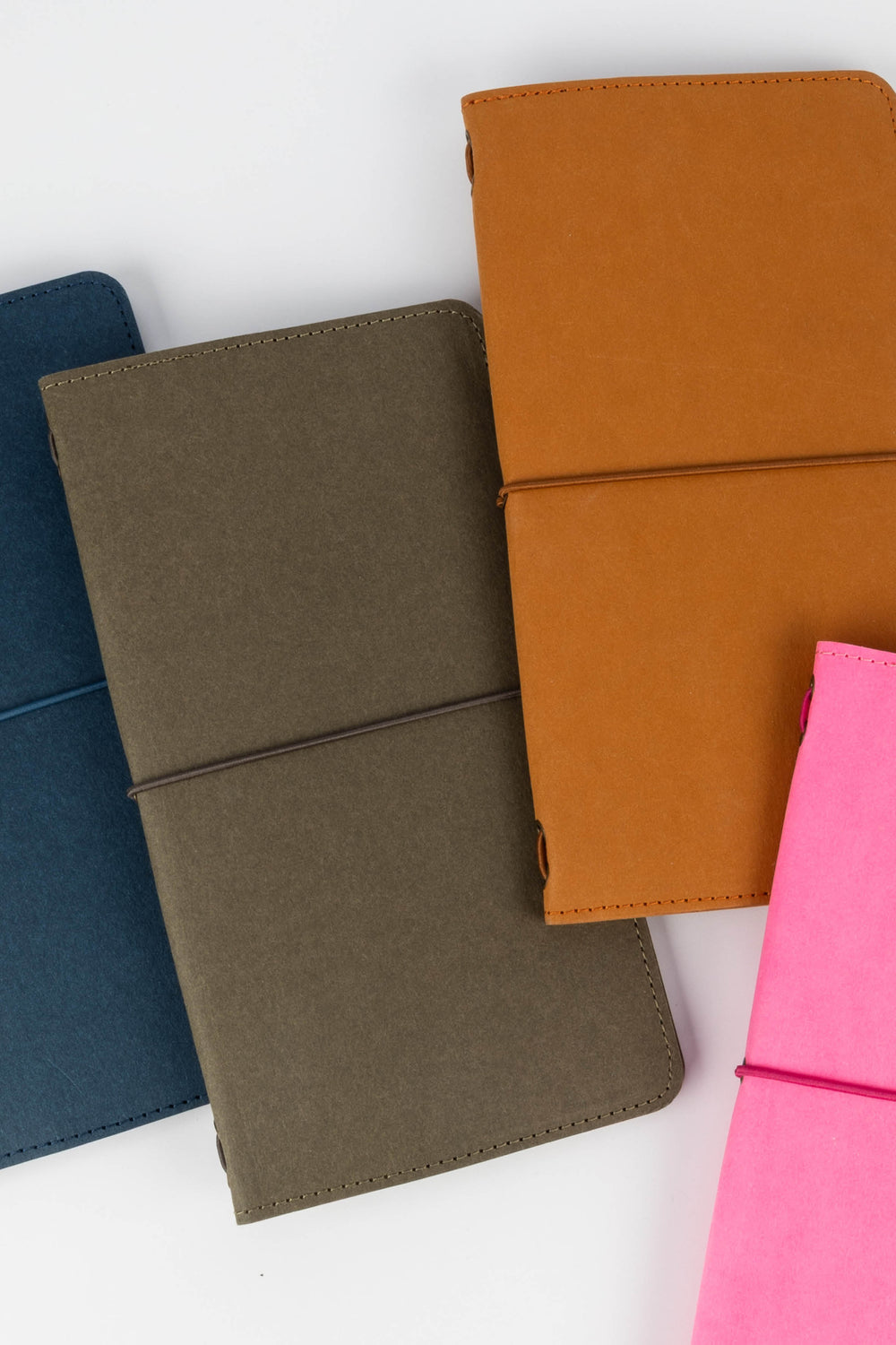 Four colourful sketch journals (blue, brown, pink, and green) on a white background