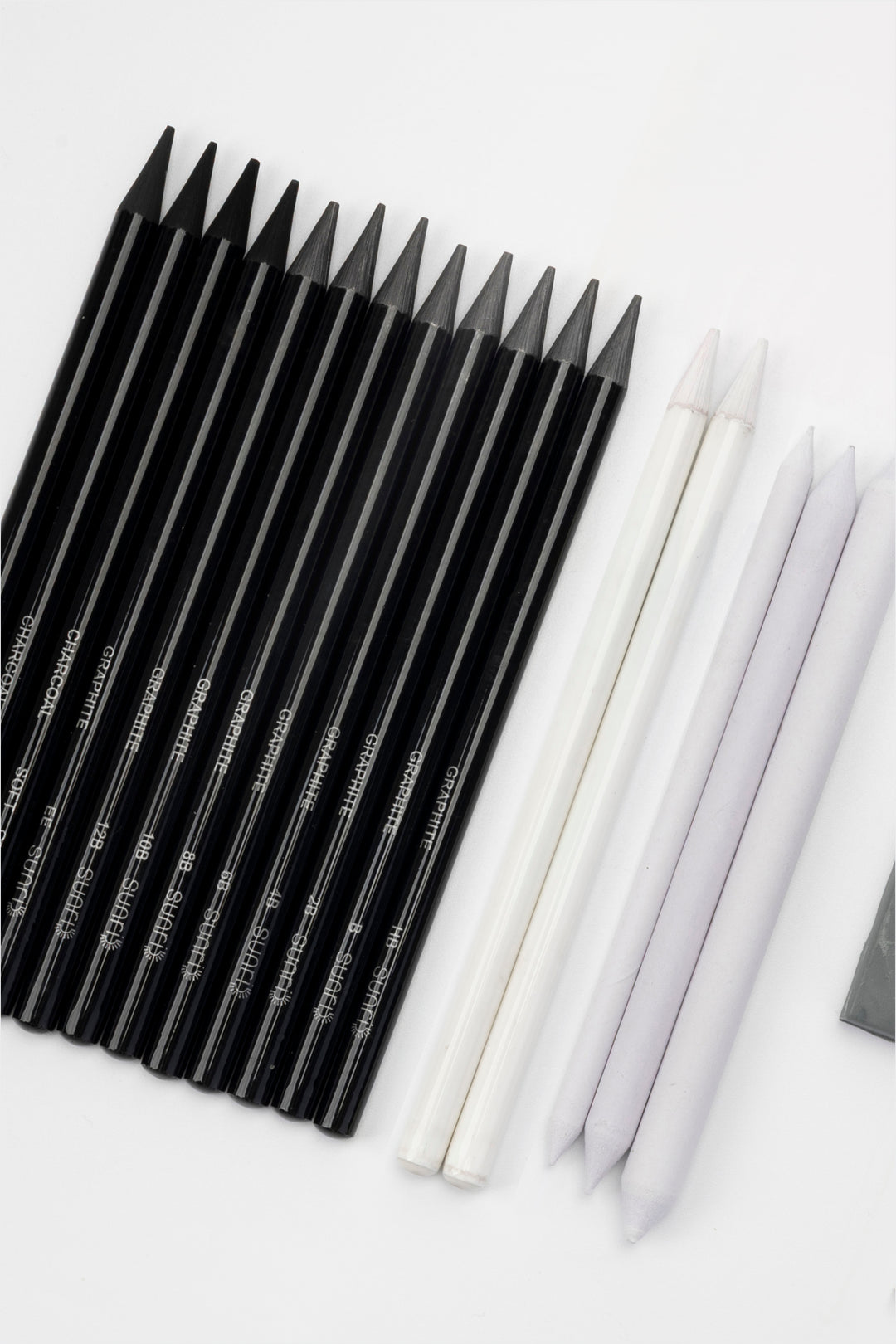 black woodless graphite sketching pencil set arranged diagonally with white blending stumps and eraser visible
