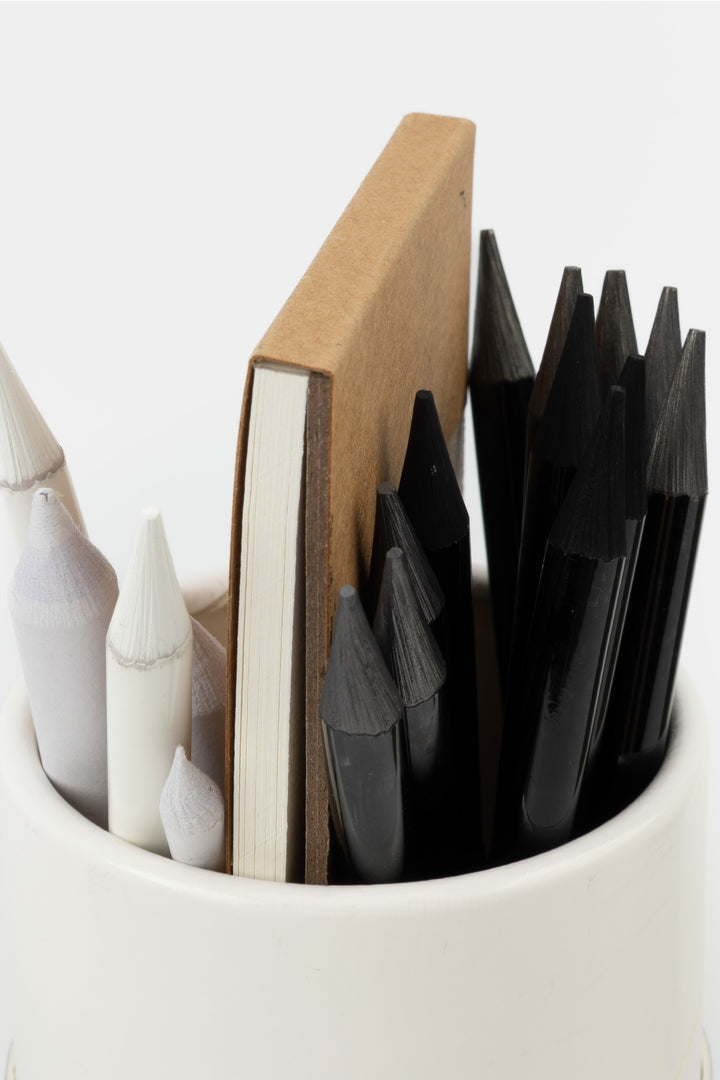 Collection of black and white ceramic vases in a white container with a wooden block.