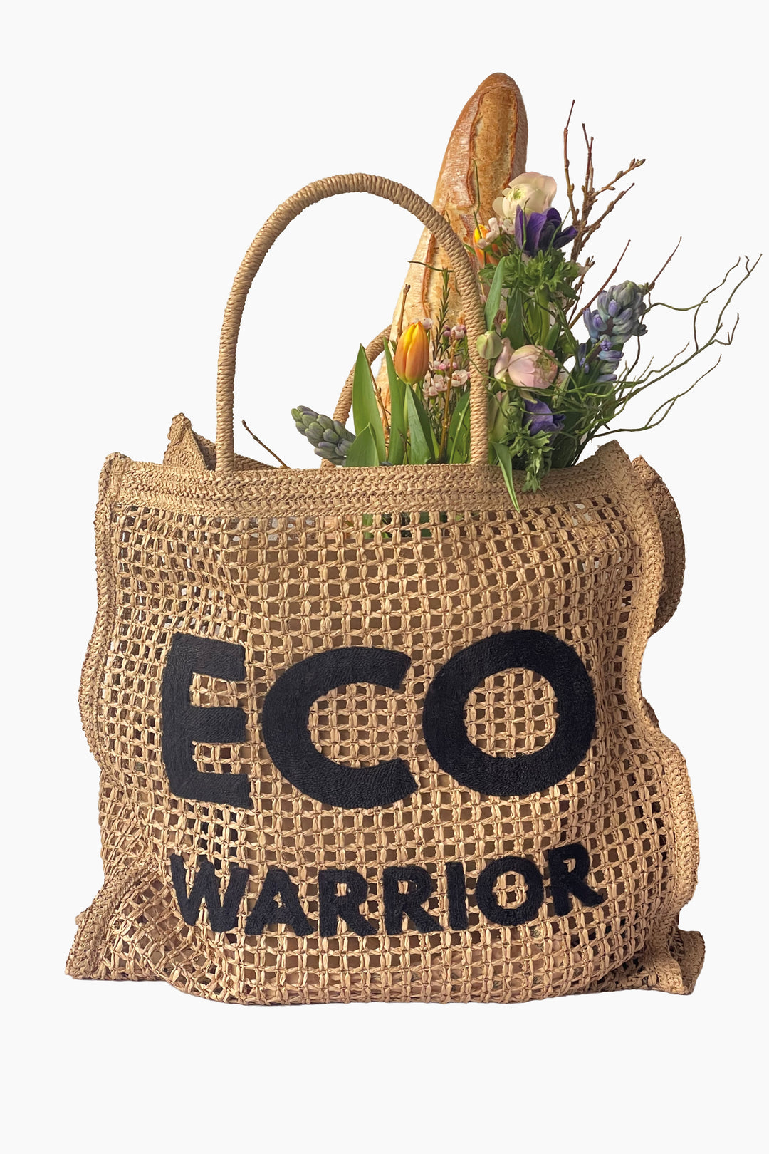 woven paper straw bag with 'ECO WARRIOR' text filled with groceries on a white background