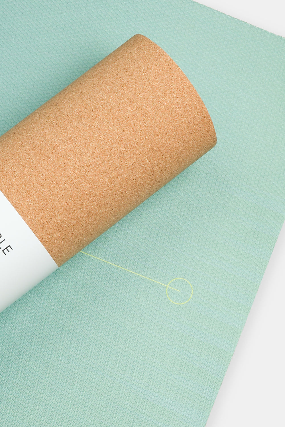 close up of ombre green yoga mat surface with alignment circle partially covered by rolled cork backing
