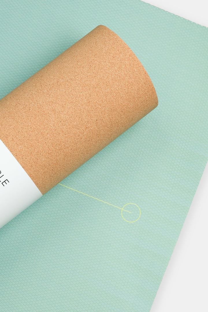 close up of ombre green yoga mat surface with alignment circle partially covered by rolled cork backing
