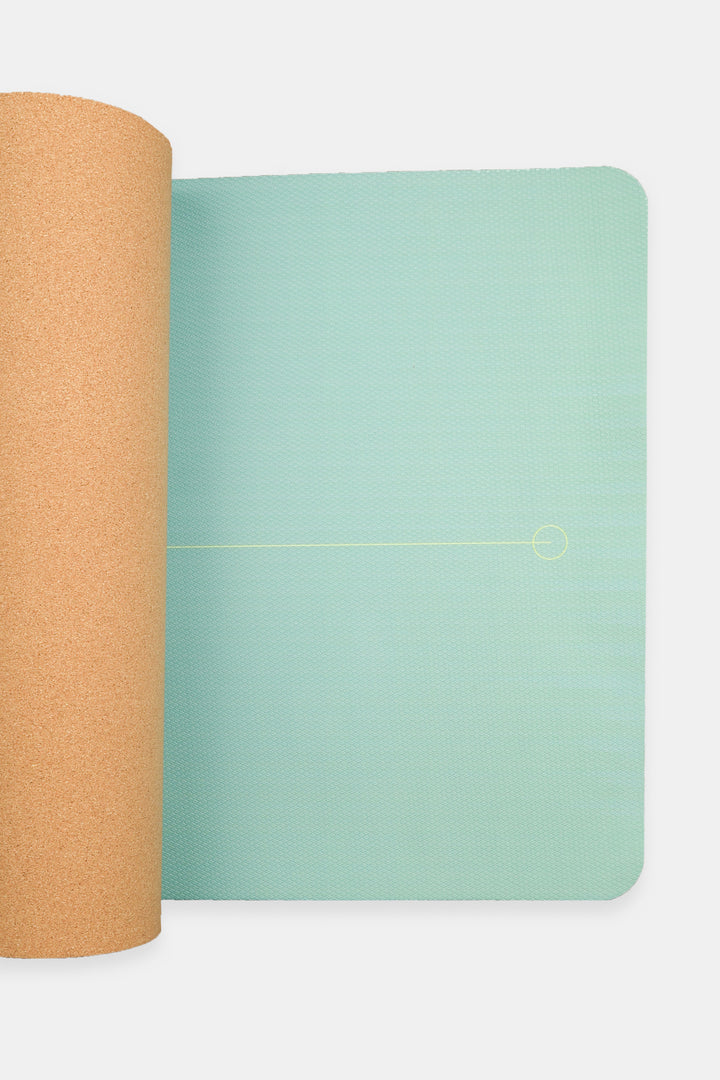 yoga mat half unrolled with ombre green gradient and alignment line visible next to cork backing
